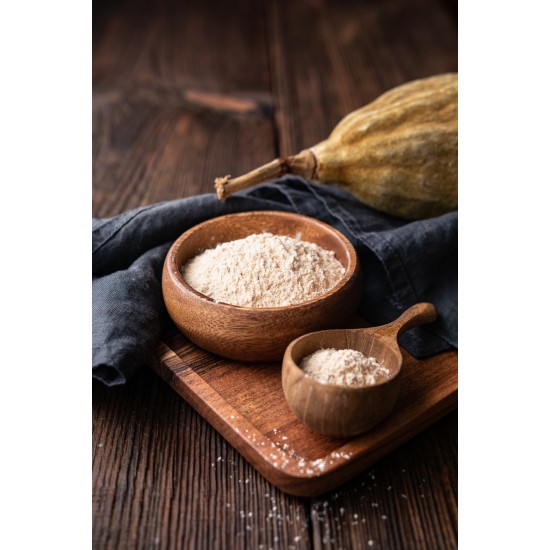 Ciotola e cucchiaio in legno contenenti polvere di baobab su tavolo in legno con frutto di baobab sullo sfondo.