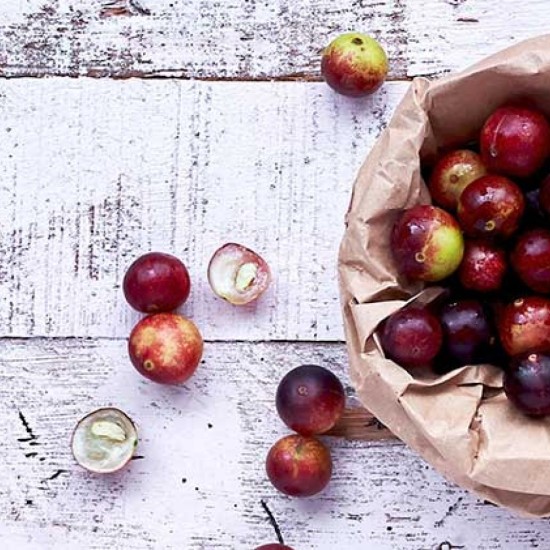 Frutti freschi di Camu Camu (Myrciaria dubia) raccolti in sacchetto di carta su superficie in legno chiaro, bacca amazzonica utilizzata nei prodotti naturali Erbologica Amazonas Andes.