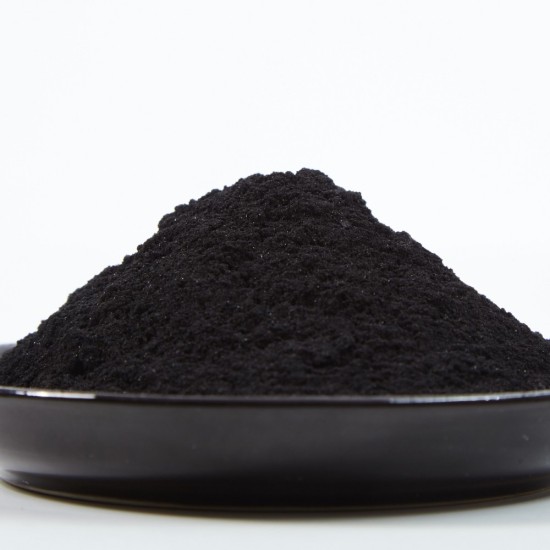 Primo piano di carbone vegetale in polvere fine di colore nero disposto su un piatto scuro con sfondo chiaro.
